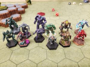 A photo depicting mech miniatures on a hex map. From left to right: Shadow Hawk and Centurion, Nightsky and Spider, Banshee and Wasp, Wolverine and Wasp, Axman and Spider, Wraith and Spider.